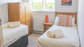 Une chambre avec deux lits, une armoire en bois, un radiateur et une fenêtre donnant sur un paysage verdoyant.