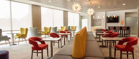 A modern restaurant with a long counter, multiple seating options including red and yellow chairs, and a large window providing a view.