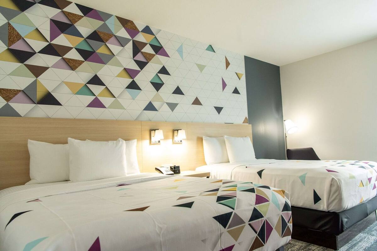 A hotel room with two beds, a geometric-patterned wall, bedside lamps, and a nightstand with a phone.