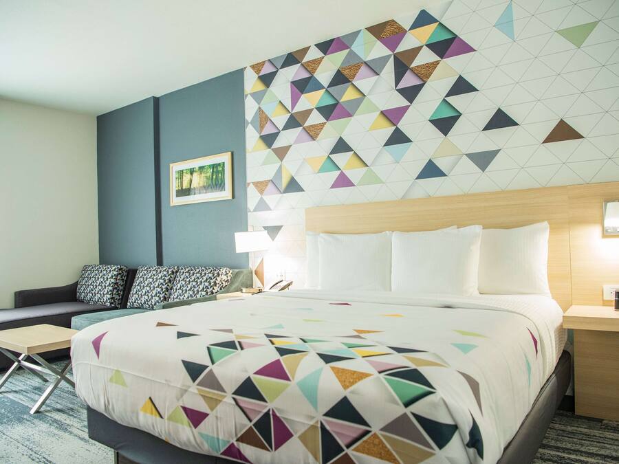 Quarto de hotel com uma cama grande, um sofá, uma escrivaninha e uma parede com padrão geométrico.