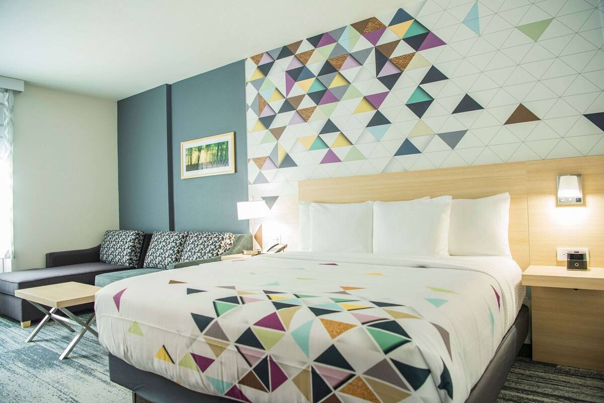 A hotel room with a large bed, a sofa, a desk, and a wall with geometric patterns.