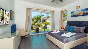 A modern hotel room with a large bed, a glass desk, and a balcony with a view of palm trees. - BEAUTIFUL 3-4 BEDROOM VILLA, PRIVATE POOL, V.I.P. ACCESS $200 per night (Puerto Plata)