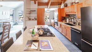 A modern kitchen with wooden cabinets, a stainless steel refrigerator, and a dining area with a table and chairs. - Luxurious Snowmass Village 3BR Condo with Amazing Views and Hot Tub on Bus Route (Snowmass Village)