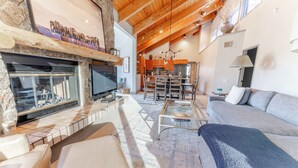 A spacious living area with a fireplace, a sofa, a coffee table, and a dining area with a chandelier. - Luxurious Snowmass Village 3BR Condo with Amazing Views and Hot Tub on Bus Route (Snowmass Village)