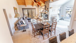A spacious living area with a wooden ceiling, a dining table with chairs, a sofa, and a large window offering a view of the outdoors. - Luxurious Snowmass Village 3BR Condo with Amazing Views and Hot Tub on Bus Route (Snowmass Village)