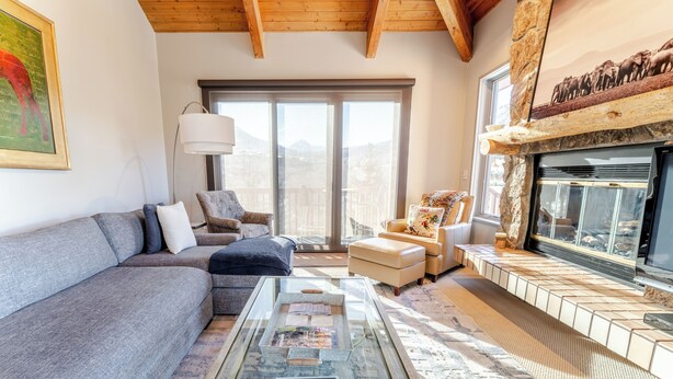 A modern living room with a stone fireplace, a large window offering a mountain view, and a cozy seating area with a sofa and armchairs. - Luxurious Snowmass Village 3BR Condo with Amazing Views and Hot Tub on Bus Route (Snowmass Village)