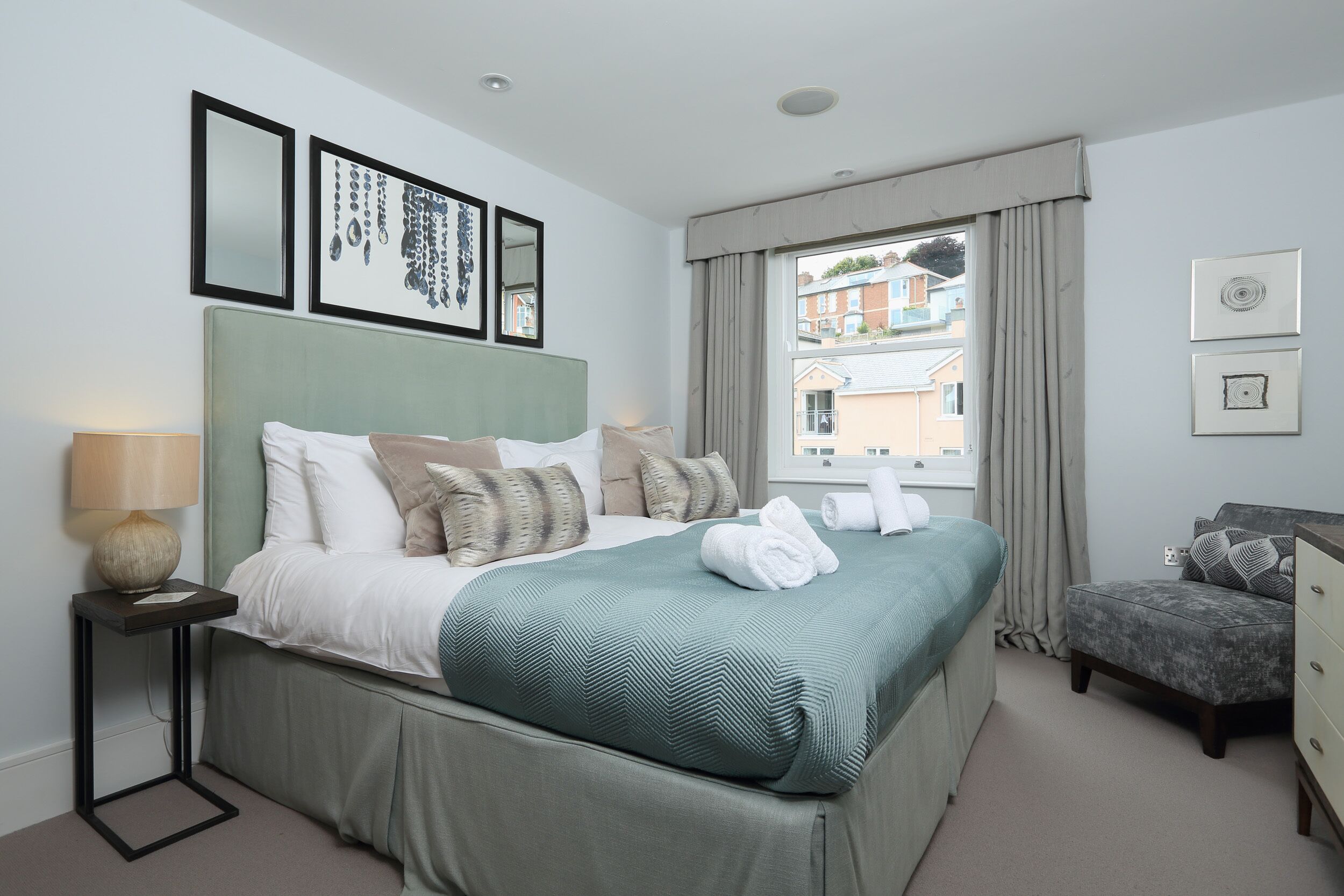 A neatly arranged bedroom with a bed, bedside table, and a view of the outside.