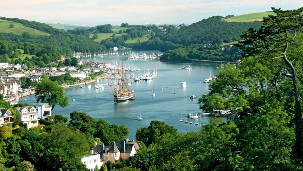 A coastal town with a marina filled with boats, surrounded by lush green hills and residential buildings. - Fairview House (Dartmouth)