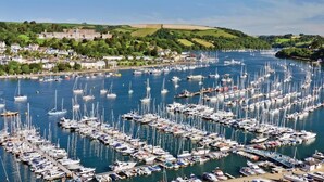 A marina filled with numerous boats, surrounded by a town with historic buildings and green hills in the background. - Fairview House (Dartmouth)