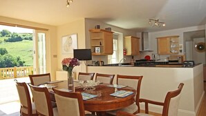 A dining area with a round wooden table and chairs, a vase with flowers, and a view of a green landscape through a glass door. - Fairview House (Dartmouth)
