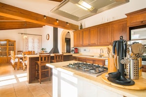 A kitchen with wooden cabinets, a central island with a stove, and a dining area with chairs and a table.