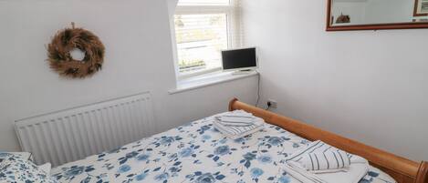 A bedroom with a bed, a window with a computer, a radiator, and a mirror on the wall.
