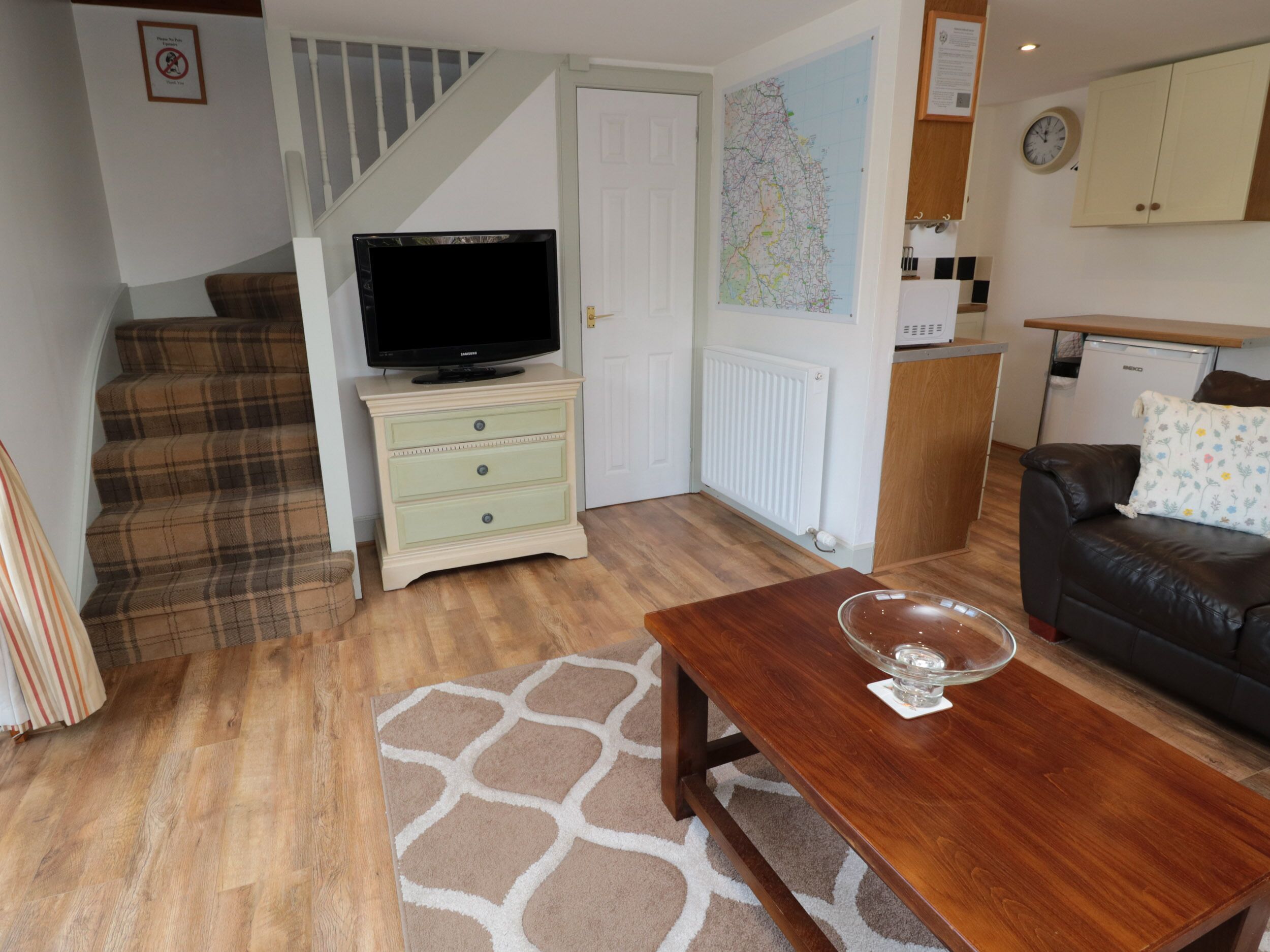 A living room with a television on a dresser, a sofa, a coffee table, and a staircase.