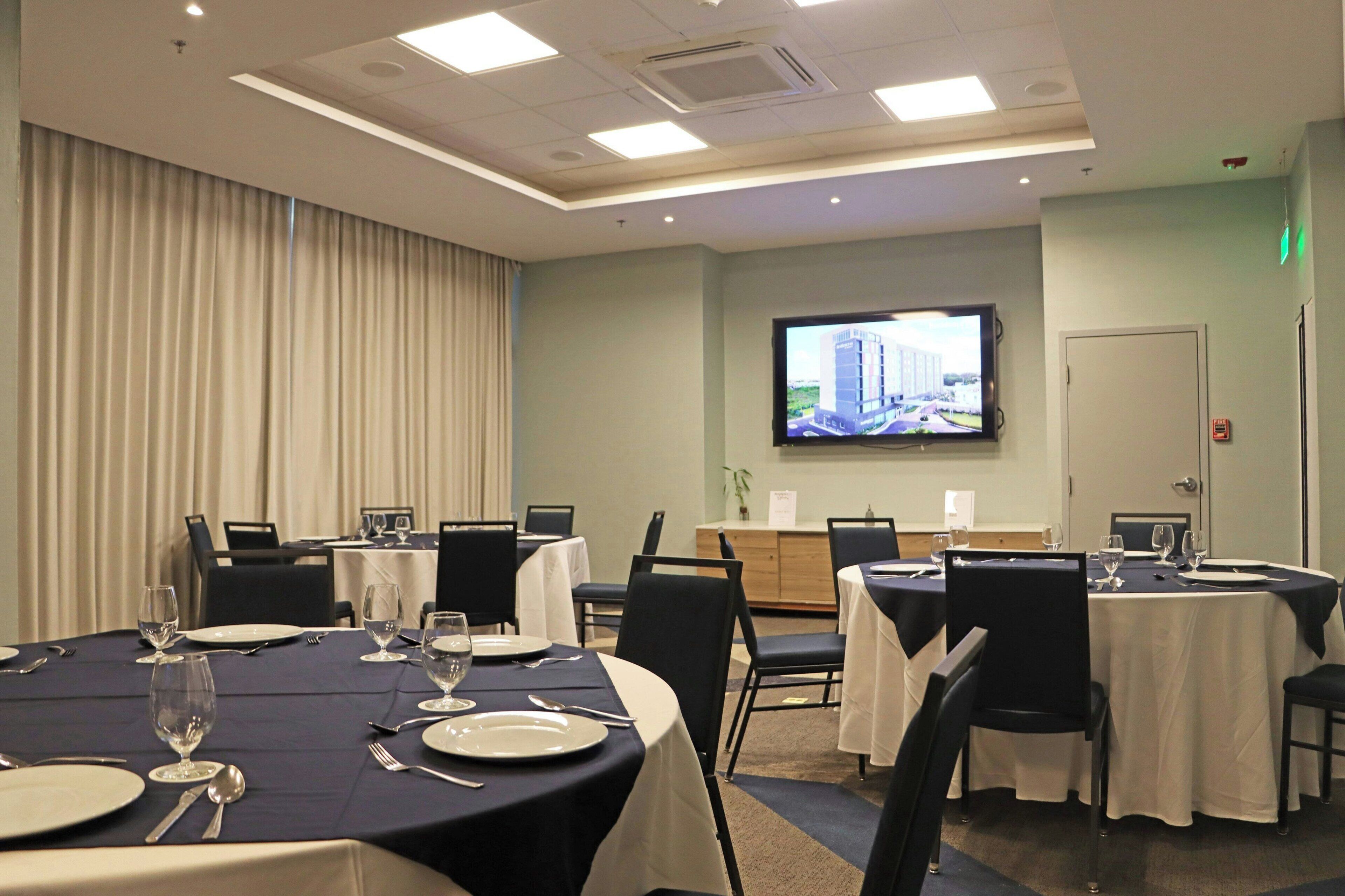 A conference room with tables set for dining, a television screen, and a door with an emergency exit sign.