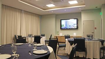 A conference room with tables set for dining, a television screen, and a door with an emergency exit sign.
