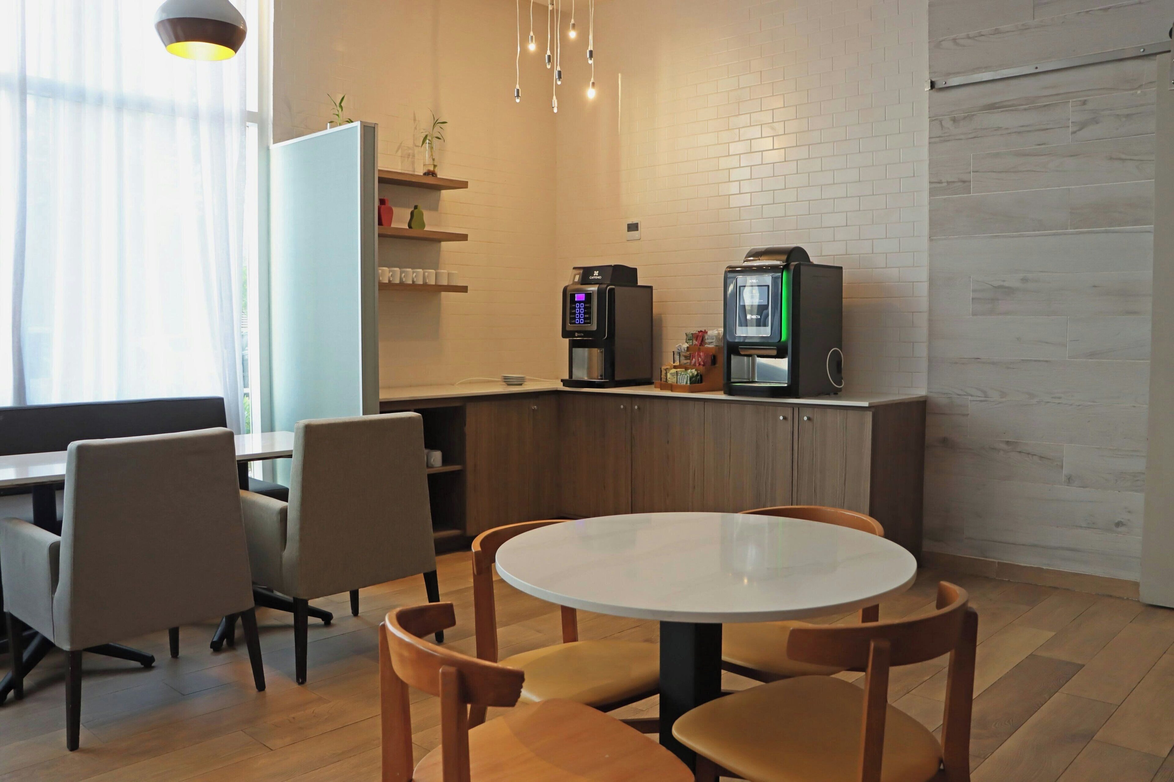 Una zona d'esmorzar modern amb una taula rodona i cadirees, una màquina de cafè i un frigorífic.