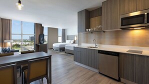 Une chambre d’hôtel moderne dotée d’un coin cuisine, d’une table à manger et d’une grande fenêtre donnant sur la ville.