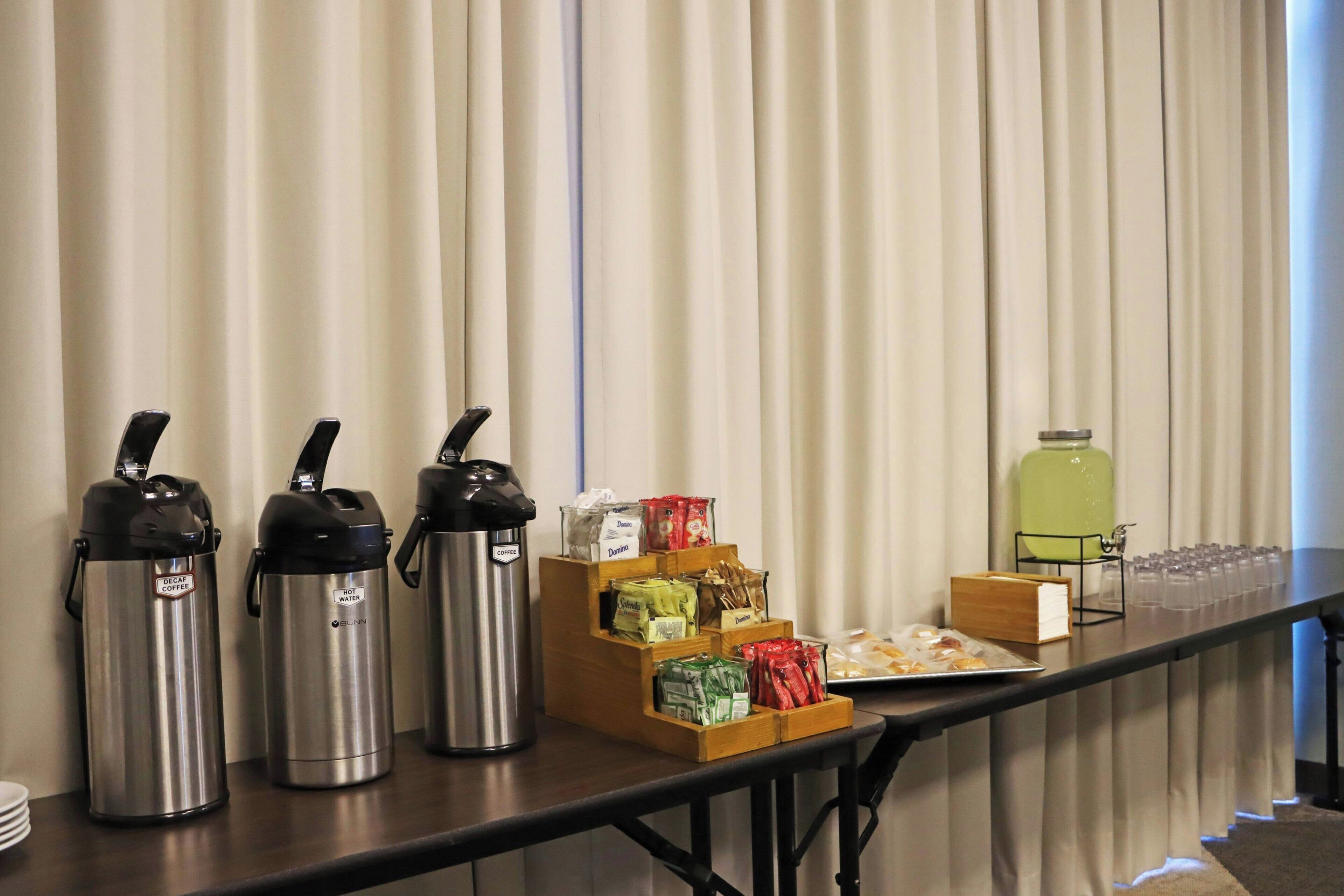 A buffet table with coffee dispensers, food items, and a water dispenser.