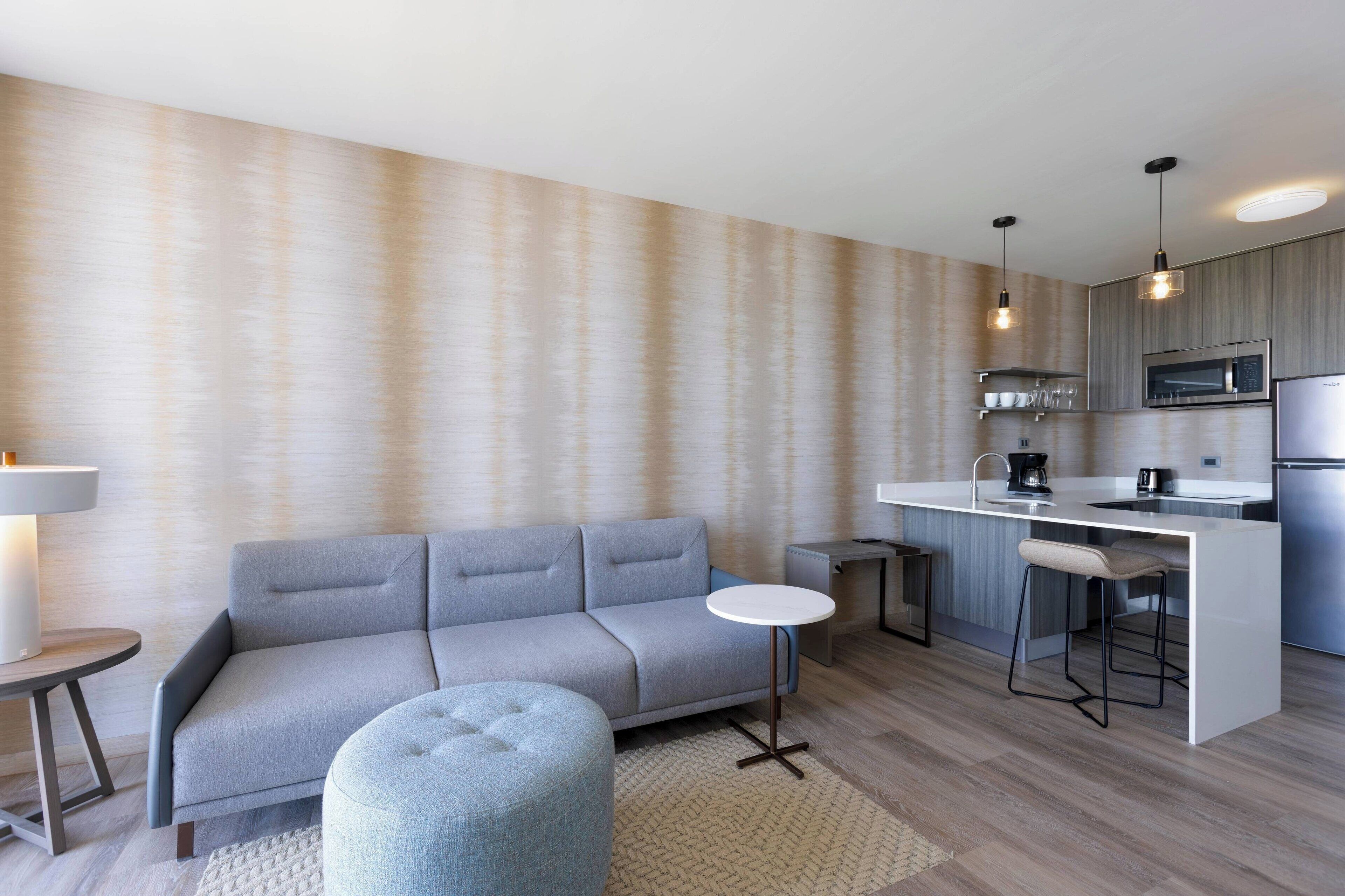 Una cocina moderna con un sofá gris, una mesa redonda y una zona de bar con taburetes.