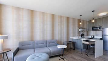 A modern kitchen with a grey sofa, a round table, and a bar area with stools.
