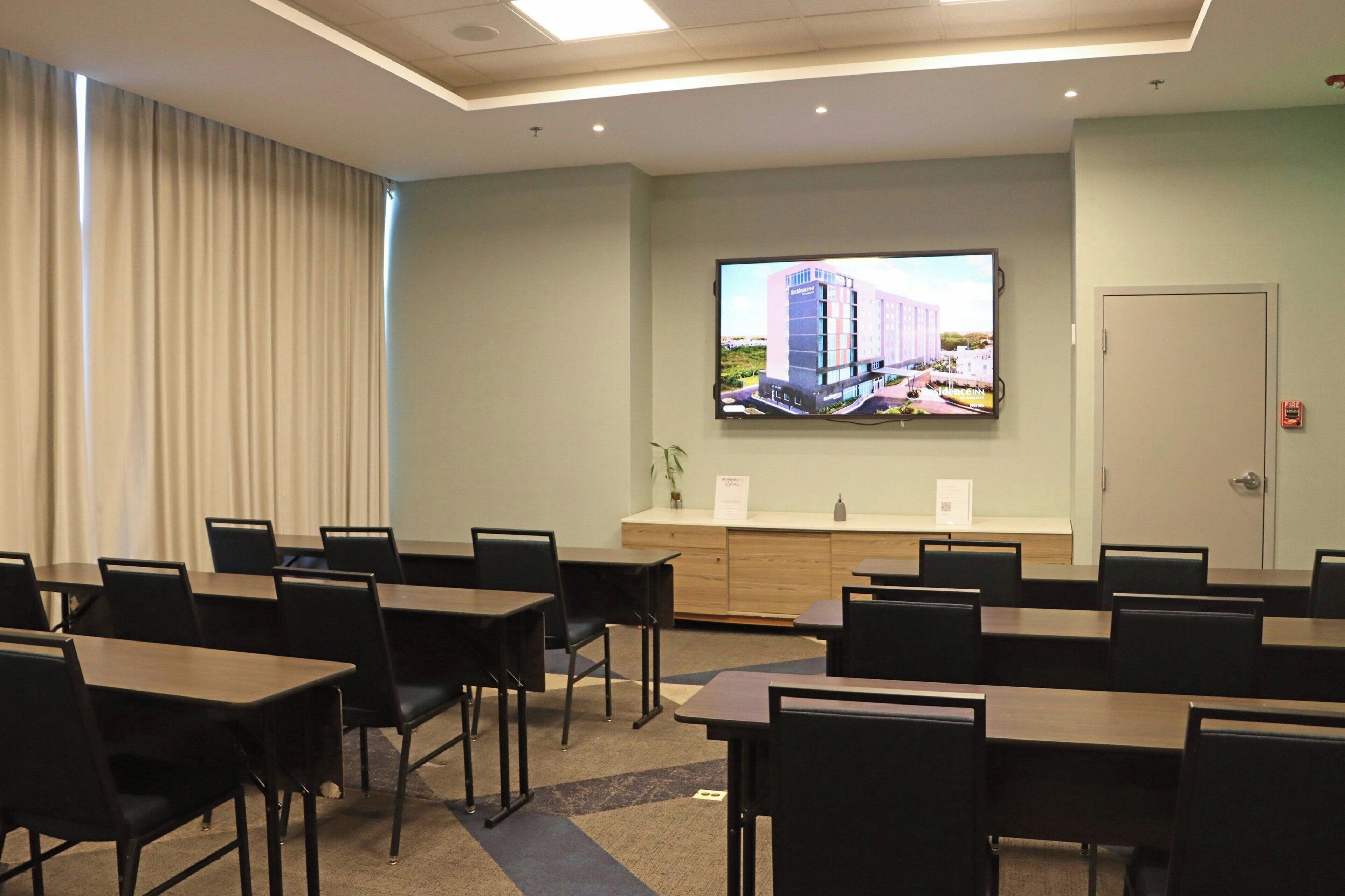 A conference room with tables and chairs, a large screen on the wall, and a door.