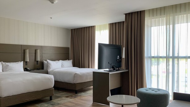 Une chambre d’hôtel avec deux lits, un bureau doté d’un téléviseur à écran plat, une petite table ronde et un pouf vert.