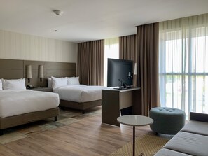 A hotel room with two beds, a desk with a flat-screen TV, a small round table, and a green ottoman. - Residence Inn by Marriott Merida (Mérida)