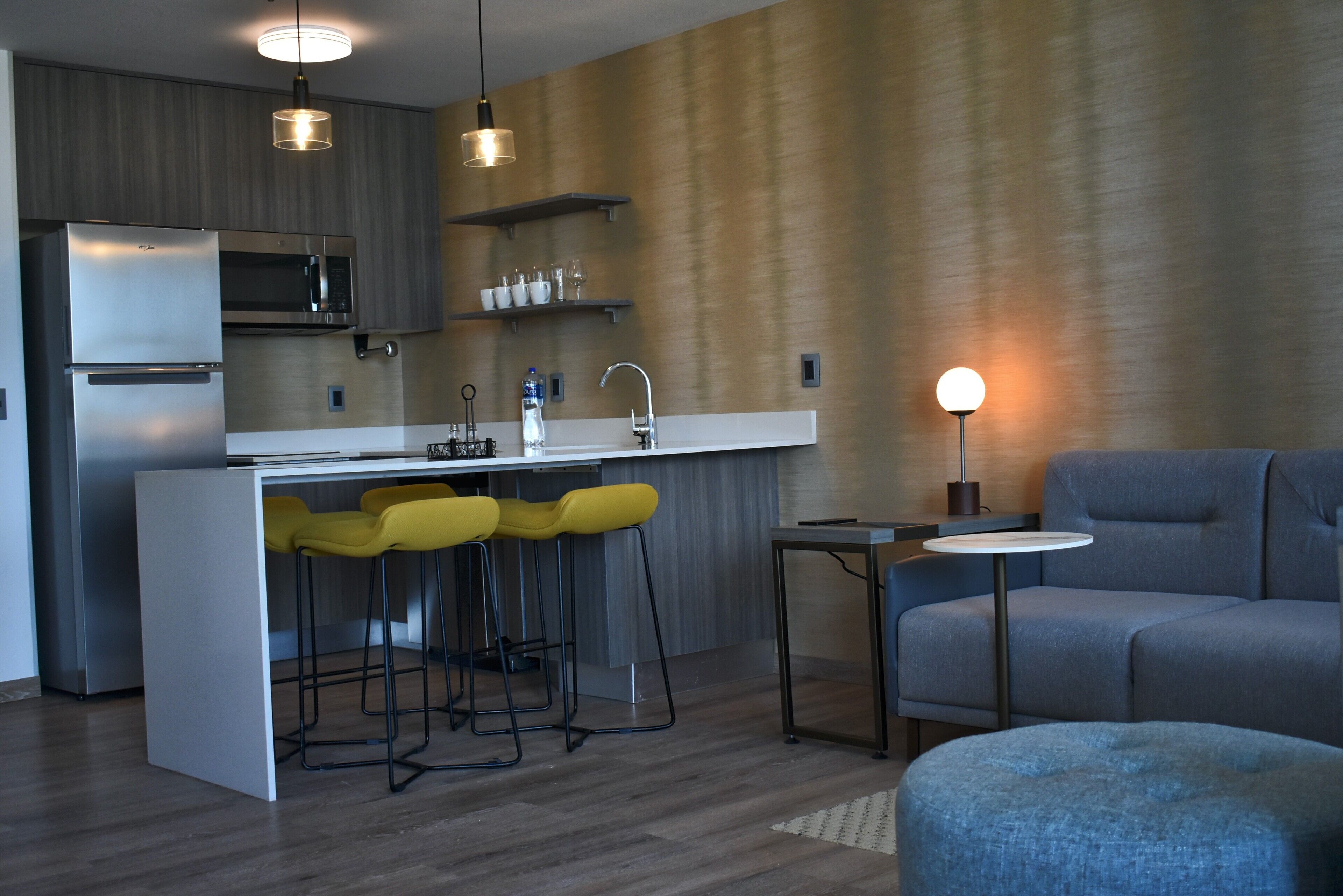 A modern kitchen with a built-in microwave, a stainless steel refrigerator, and a bar area with yellow stools.