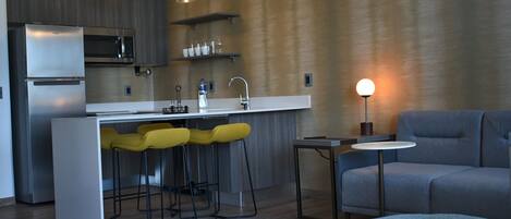 A modern kitchen with a built-in microwave, a stainless steel refrigerator, and a bar area with yellow stools.