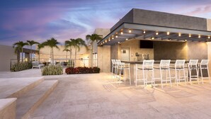 Un espace extérieur aménagé en terrasse, avec un bar et des sièges, entouré de palmiers et de plantes.