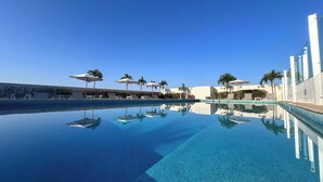 A clear blue infinity pool with lounge chairs and umbrellas, surrounded by modern buildings and palm trees. - Residence Inn by Marriott Merida (Mérida)
