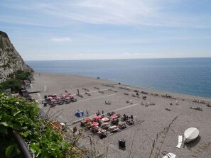 Una playa con mesas de picnic y sombrillas, un acantilado rocoso y el mar.