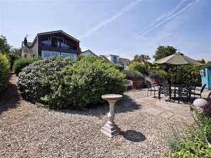 Un jardin avec un espace patio, un abreuvoir pour oiseaux et un petit abri de jardin.