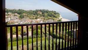 En balkon med udsigt over en kystby, grønt og en sandstrand.