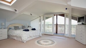 Et soveværelse med seng, natbord, kommode, et vindue og en balkon.