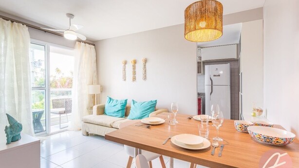 A modern dining area with a wooden table set for four, a ceiling fan, and a decorative hanging light fixture. - Palm Village Acqua (Ipojuca)