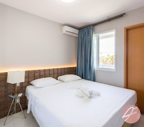Une chambre d’hôtel équipée d’un lit, d’une lampe de chevet, d’un climatiseur et d’une fenêtre avec des rideaux.