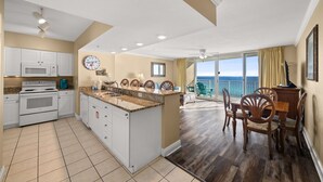 A kitchen with a central island, white cabinets, a microwave, and a stove. There is a dining area with wooden chairs and a table. - Beach front condo at Emerald Beach Resort!! (PANAMA CITY BEACH)
