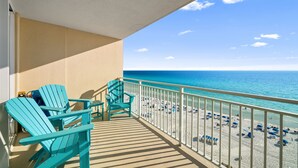 A balcony with two chairs, a table, and a view of a beach with umbrellas and people. - Beach front condo at Emerald Beach Resort!! (PANAMA CITY BEACH)