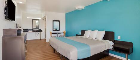 A modern hotel room with a bed, bedside table, and a desk with a chair.