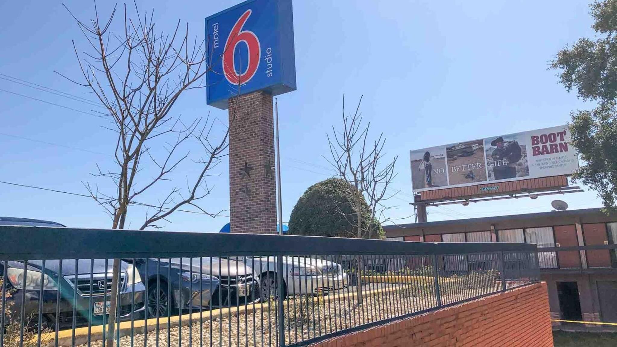 A motel sign, a parking lot with cars, and a billboard advertising a boot barn.