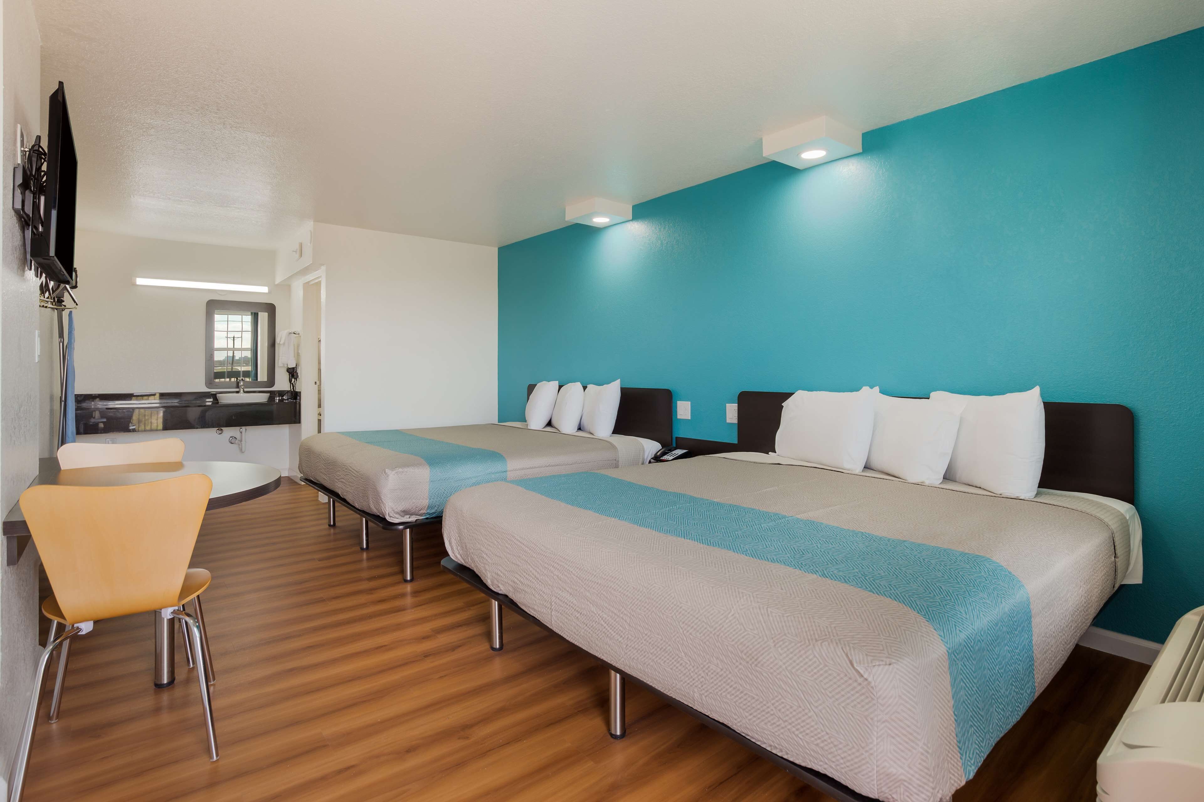 Habitación de hotel con dos camas, una mesita, una silla y un televisor.