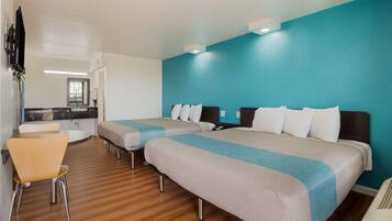 A hotel room with two beds, a small table, a chair, and a TV.