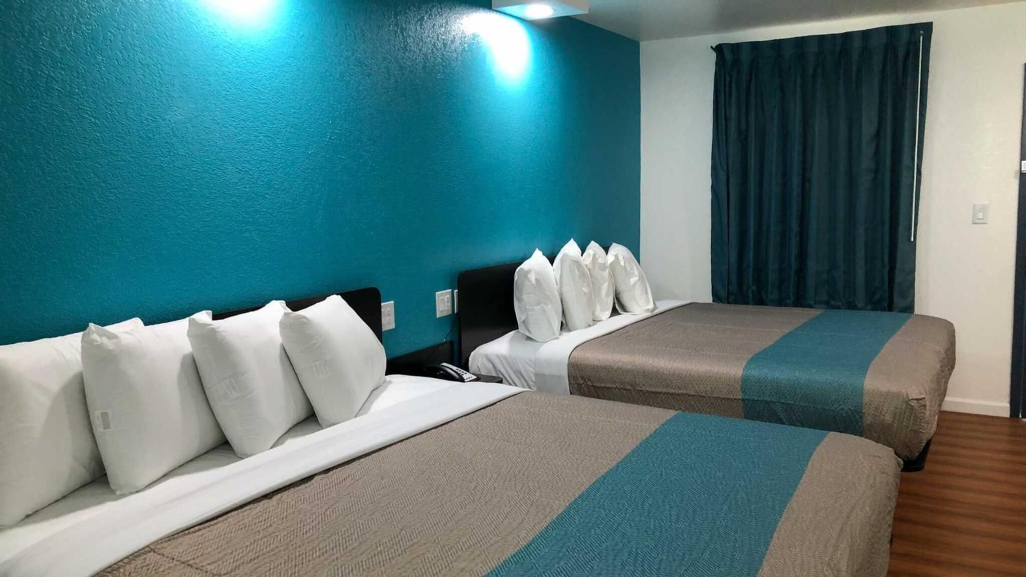 A hotel room with two beds, teal walls, and a dark curtain.