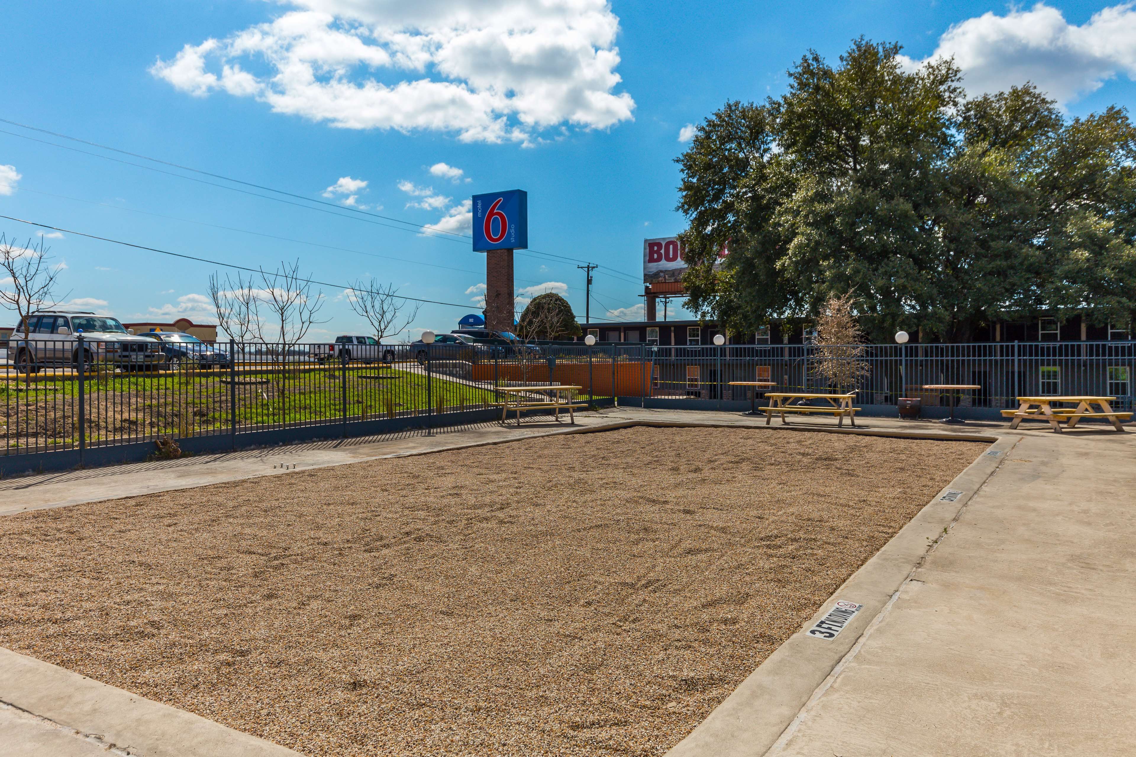 A parking lot with a 6 Motel sign, picnic tables, and a fenced area.