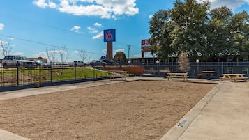 A parking lot with a 6 Motel sign, picnic tables, and a fenced area.