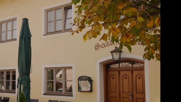 A building with a large wooden door, a green umbrella, and outdoor seating. - Gasthof Feldl (Bergkirchen)