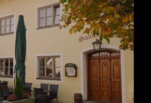 A building with a large wooden door, a green umbrella, and outdoor seating. - Gasthof Feldl (Bergkirchen)
