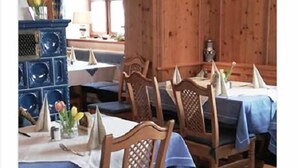 A dining area with wooden chairs and tables, a stone fireplace, and wooden paneling on the walls. - Gasthof Feldl (Bergkirchen)