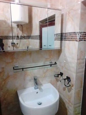 Une salle de bain avec un lavabo blanc, un miroir au-dessus et un mur recouvert de carreaux derrière le lavabo.